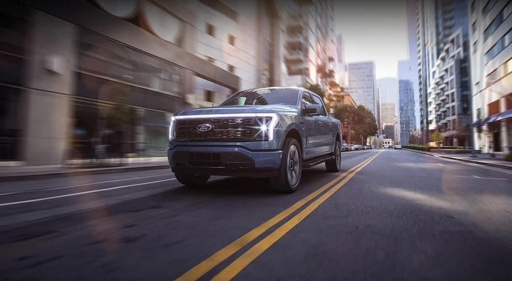 A blue 2024 Ford F-150 Lightning for sale is shown driving on a city street