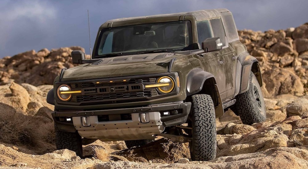 A dark green 2024 Ford Bronco Raptor driving over rocks in a desert