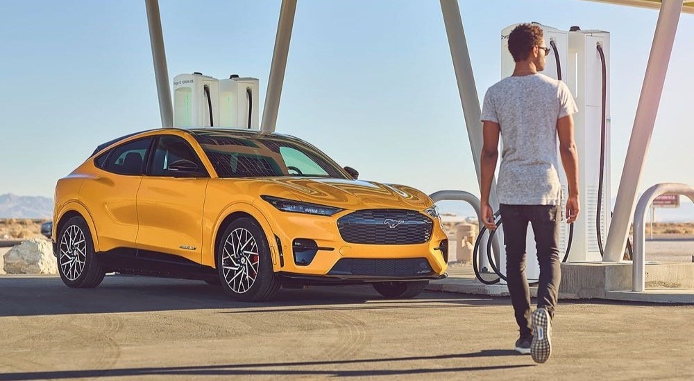 A man walking towards a yellow 2025 Ford Mustang Mach-E for sale in Rhinebeck parked at a charging station