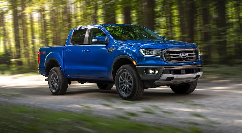 Blue Ford Ranger pickup truck driving on a forest road with blurred green trees in the background