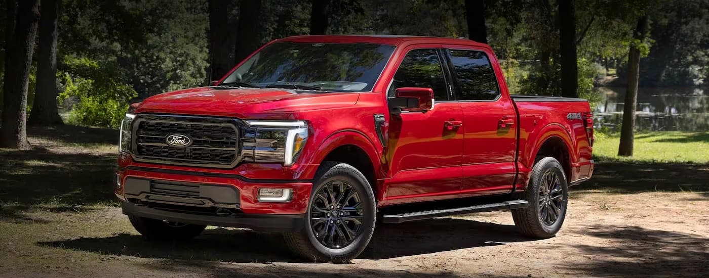 Red 2023 Ford F-150 parked off-road near a forest.