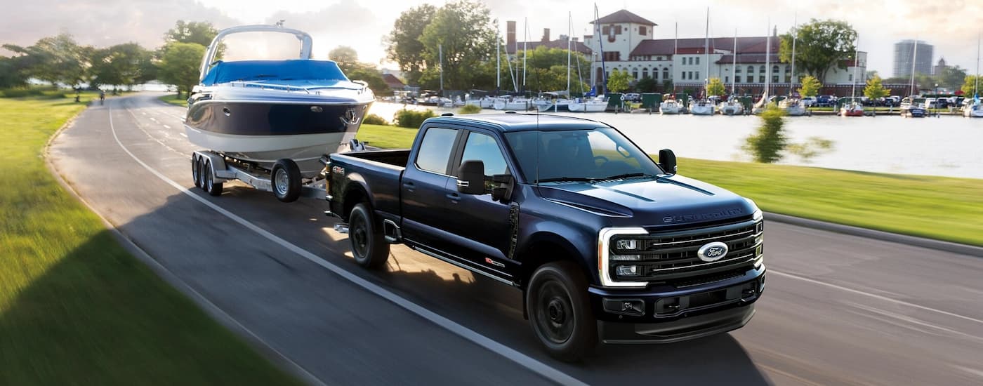 Black 2025 Ford F-350 towing a boat down a road from a dealer with trucks for sale.