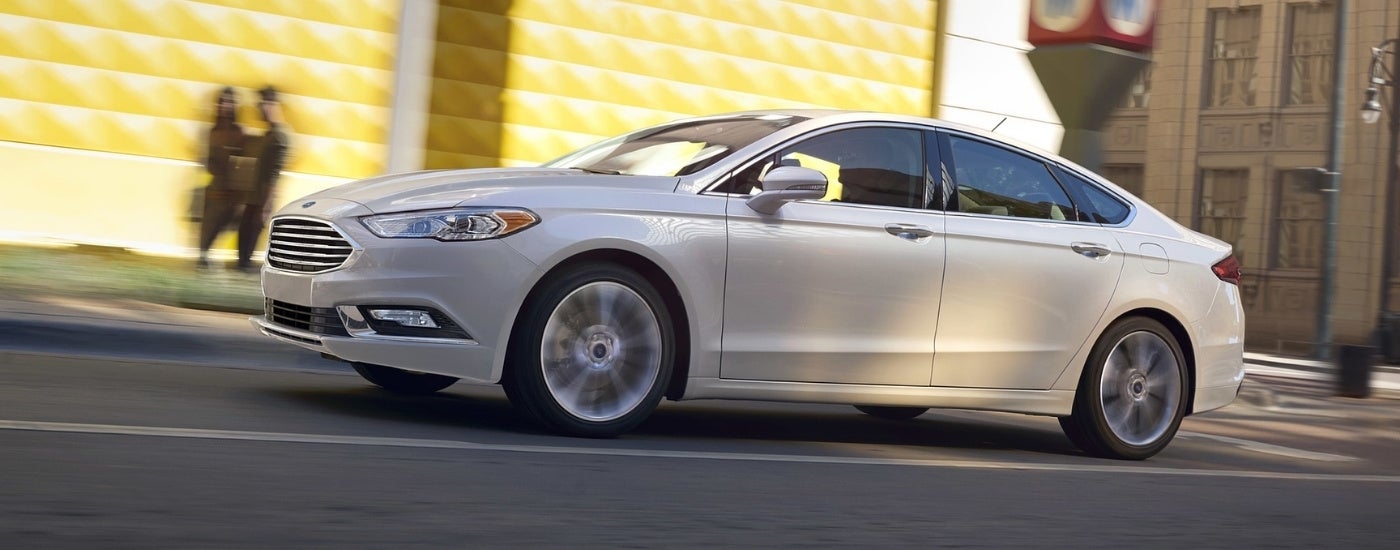 A white 2018 Ford Fusion driving to a used car dealer.