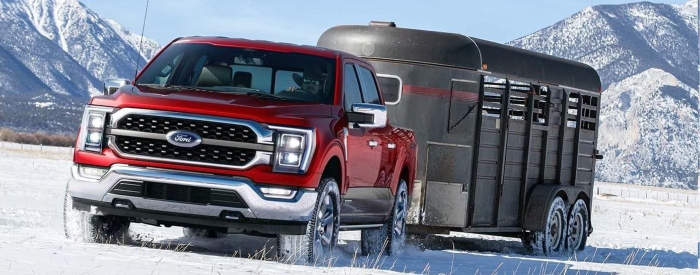 A red 2022 used Ford F-150 for sale near Rhinebeck is towing a trailer on snow.