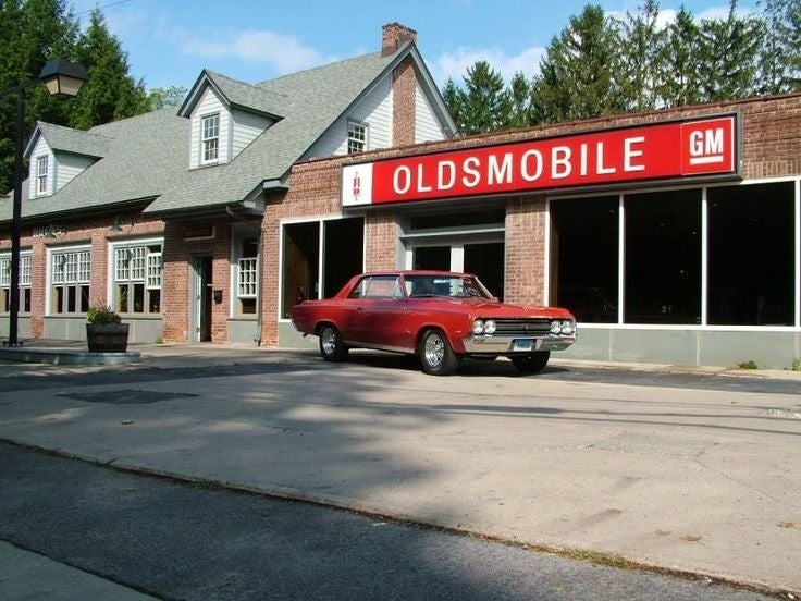 Restored brick Oldsmobile dealership with a classic red car parked outside.