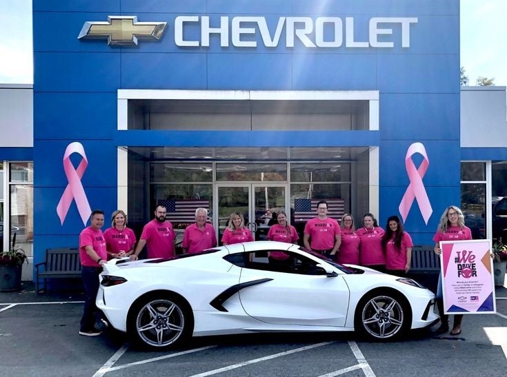 Chevrolet dealership team in pink shirts standing behind a white sports car