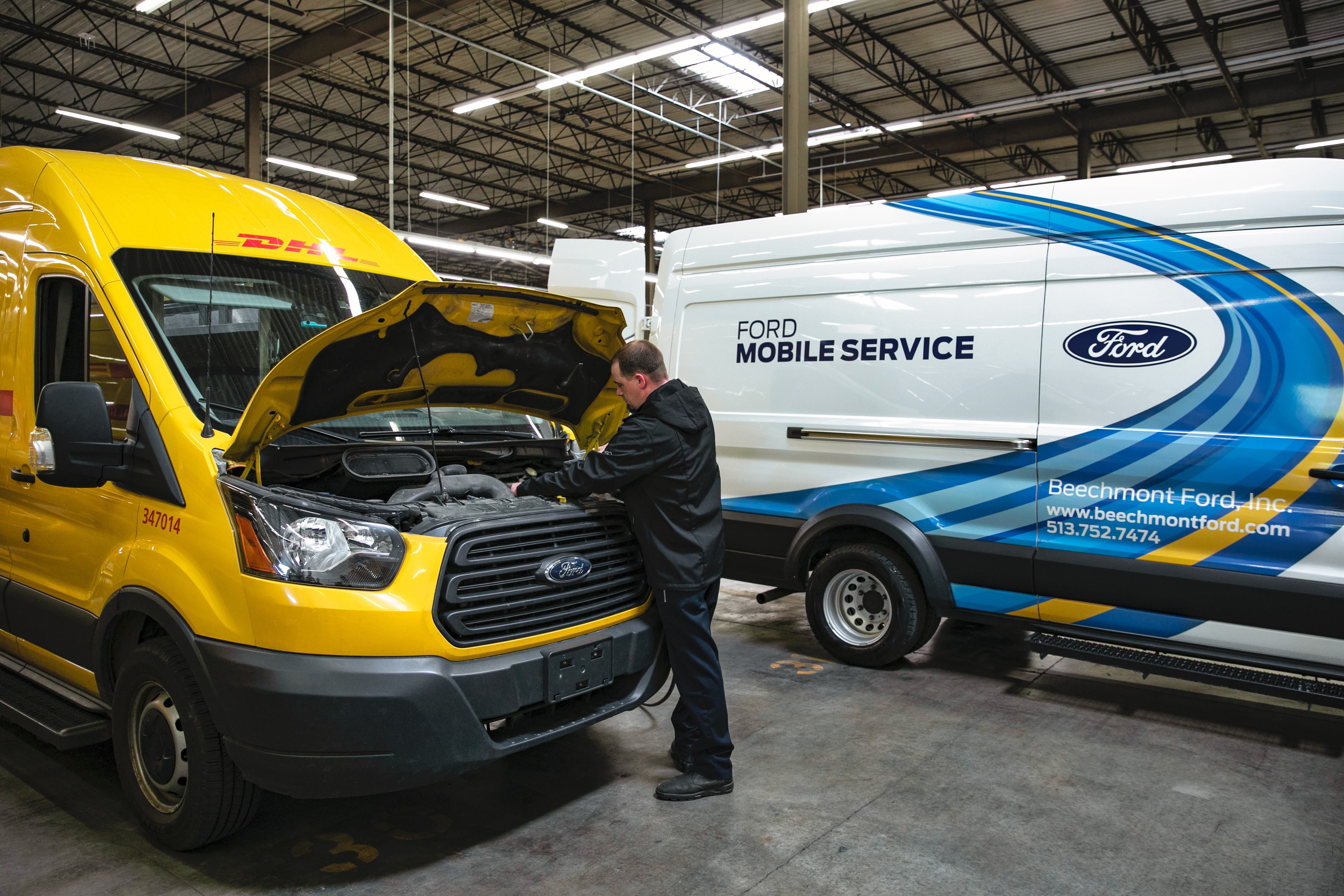 A worker servicing a yellow van beside a Ford Mobile Service van.