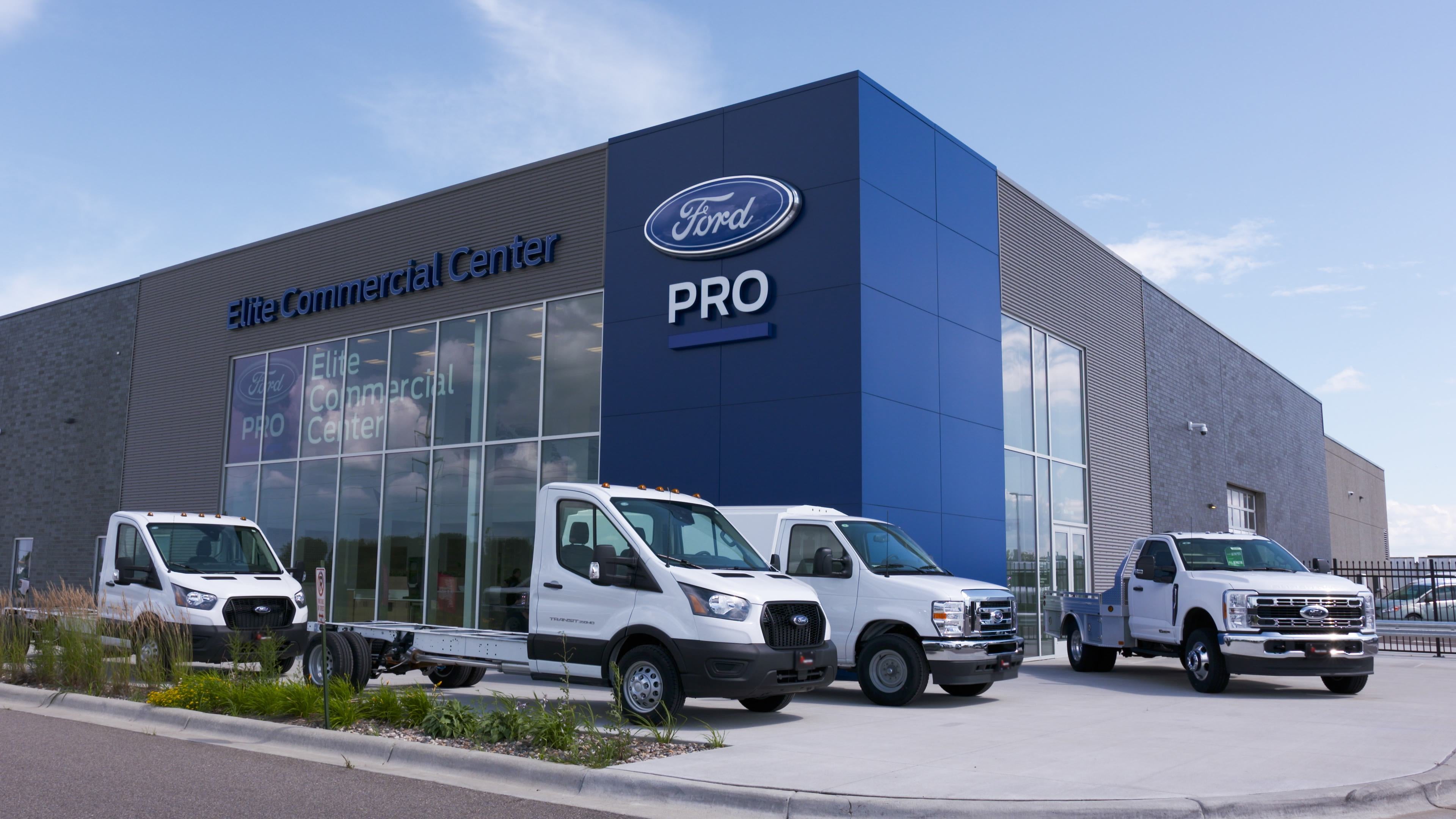 A Ford Elite Commercial Center with several white Ford commercial vans and a flatbed truck.
