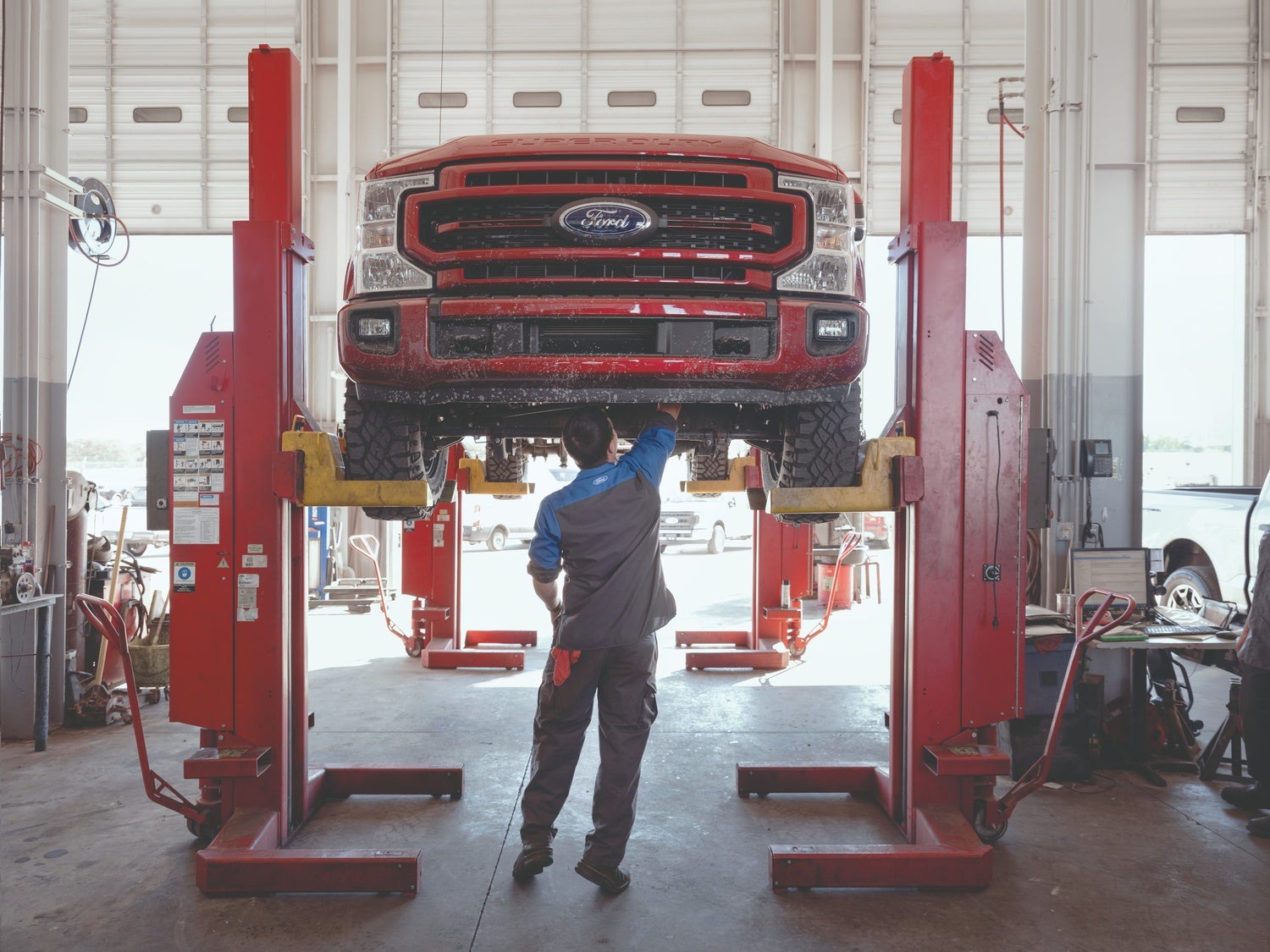 A technician working under a lifted red Ford truck.